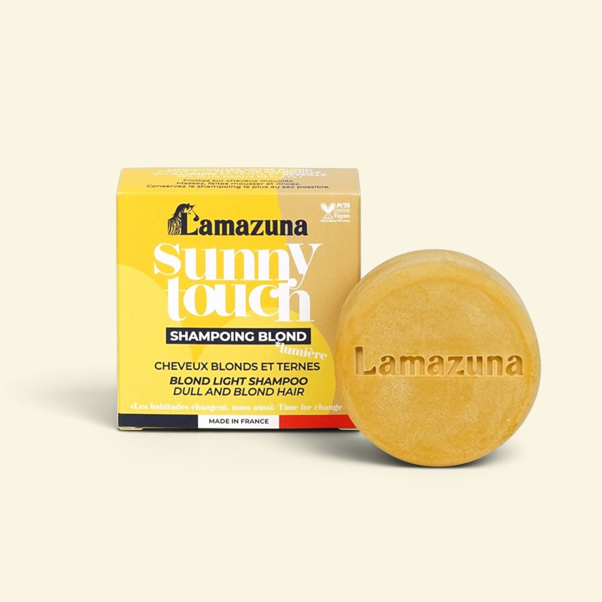 Lamazuna Sunny Touch Blond shampoo bar next to its yellow packaging box on a light cream background.